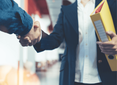Close-up of professionals shaking hands while holding documents, symbolizing successful business partnership