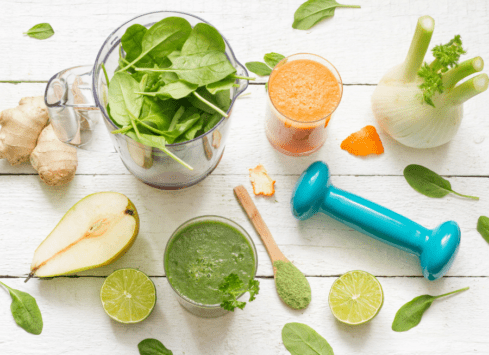 Healthy green smoothie ingredients: spinach, pear, lime, ginger, and weights on white wood table