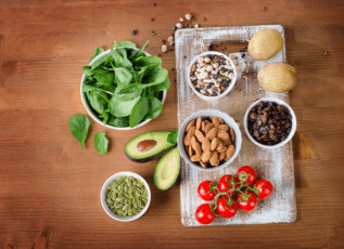 Healthy foods on a wooden table: spinach, nuts, seeds, avocado, potatoes, raisins, and tomatoes