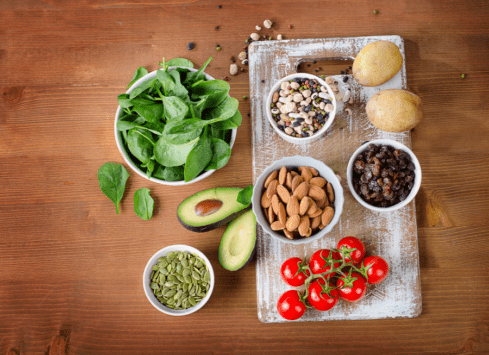 Healthy foods on a wooden table: spinach, nuts, seeds, avocado, potatoes, raisins, and tomatoes
