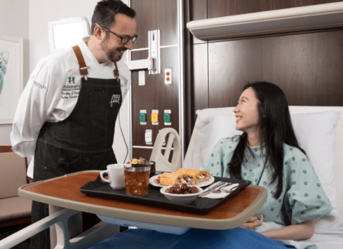 Morrison Healthcare chef and patient smiling while enjoying a meal in a hospital room