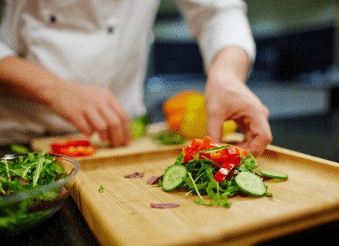 Chef preparing fresh salad with colorful vegetables on wooden cutting board in kitchen