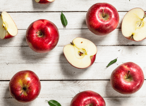 Red apples on white wooden table with leaves