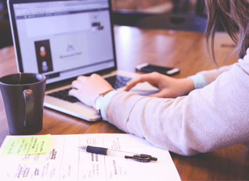 Woman working on laptop while taking notes, with coffee mug nearby