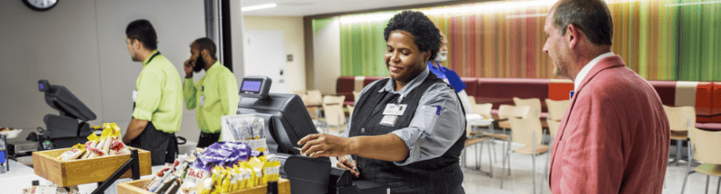 Morrison Healthcare associate assists customer at checkout in colorful hospital cafeteria