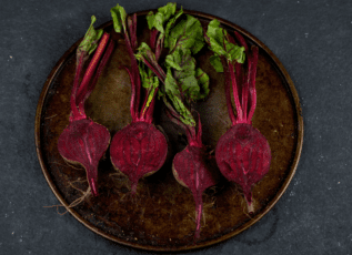 Freshly harvested red beets with green leaves on rustic plate