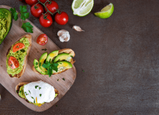 Avocado toast with poached egg, cherry tomatoes, lime, and garlic on wooden cutting board