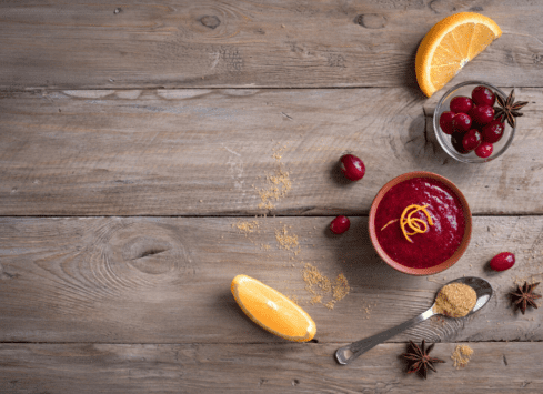 Cranberry sauce, cherries, orange slice, and spices on rustic wooden table