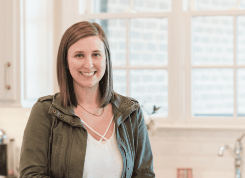 Young smiling woman in green jacket poses in kitchen setting