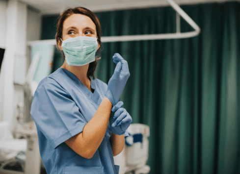 Hospital nurse putting on blue medical gloves and wearing a mask in a patient room