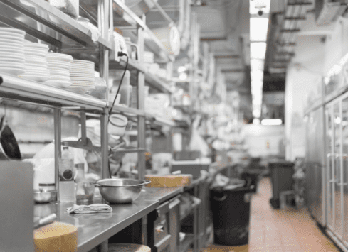 Commercial kitchen with stainless steel shelves, appliances and dishware in a narrow aisle