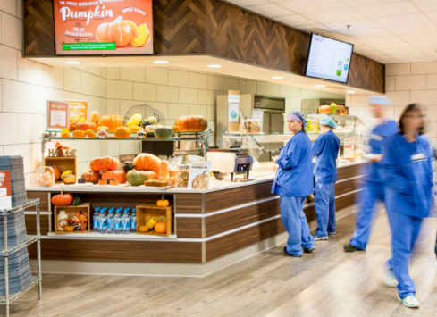 Pumpkin display at hospital cafeteria serving station with staff in blue scrubs walking by