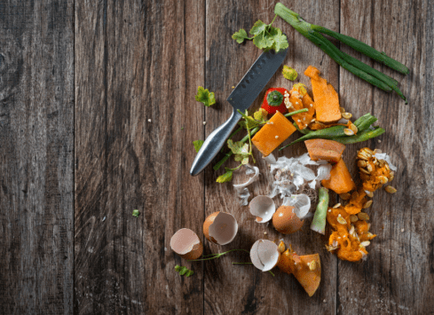 Vegetable food waste on rustic wooden table with kitchen knife and green onions