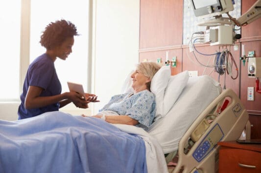 Nurse visiting smiling senior woman patient in hospital bed