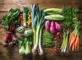 Variety of fresh vegetables on wooden table including leafy greens, carrots, beets, and leeks