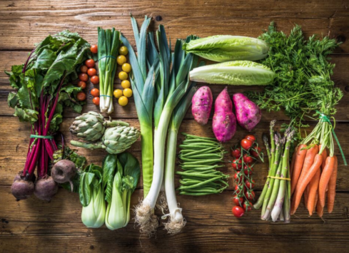 Variety of fresh vegetables on wooden table including leafy greens, carrots, beets, and leeks