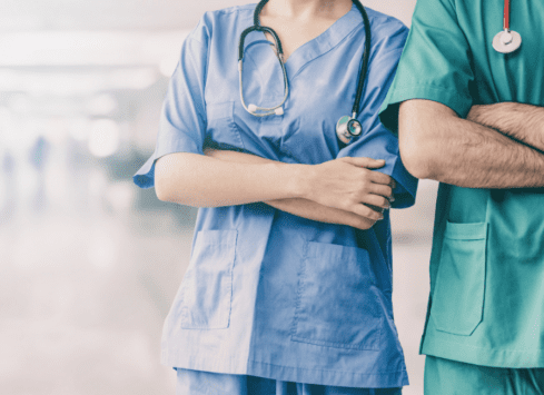 Two healthcare workers in scrubs stand together, one with arm around the other's back