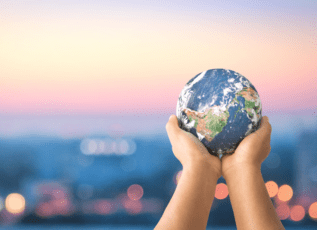 Hands holding Earth globe against blurred city lights at dusk