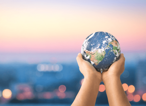 Hands holding Earth globe against blurred city lights at dusk