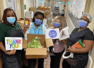 Morrison Healthcare staff wearing masks holding thank you signs and food donations in a hospital hallway