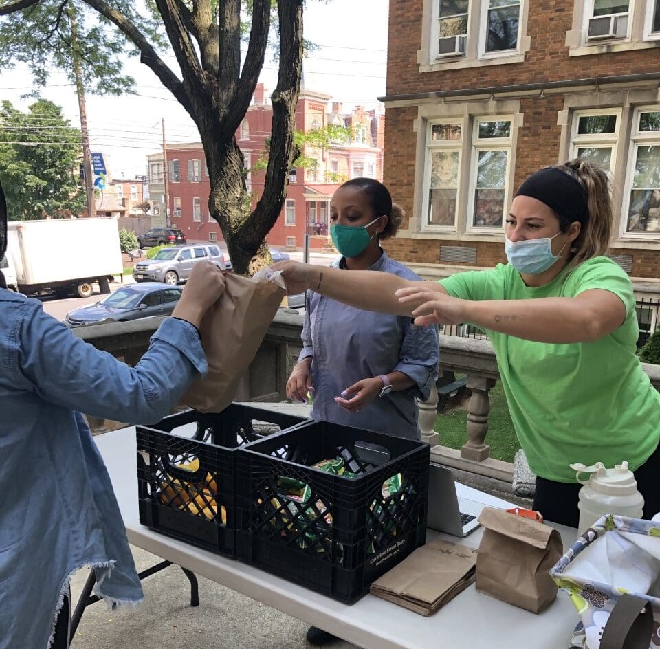 Morrison Healthcare volunteers distribute food while wearing masks on an urban street