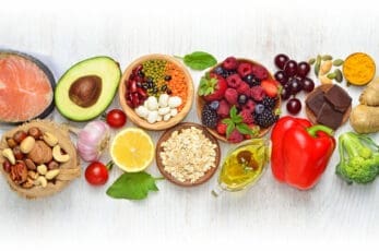 Healthy foods including fruits, vegetables, fish, nuts, seeds, avocado, lemon, olive oil, and chocolate