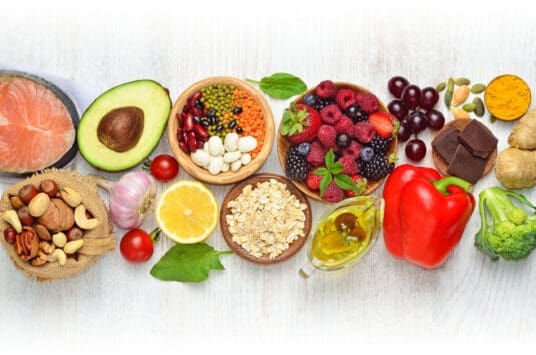 Healthy foods including fruits, vegetables, fish, nuts, seeds, avocado, lemon, olive oil, and chocolate