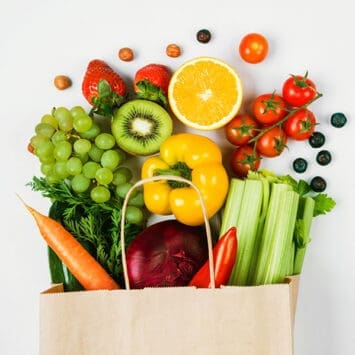 Fresh fruits and vegetables in a grocery bag including grapes, oranges, peppers, kiwi, and celery