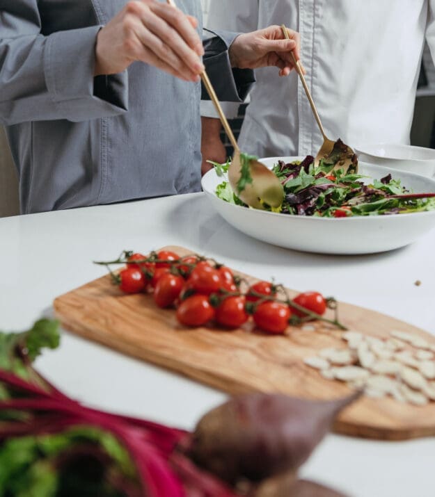 Chefs preparing a fresh salad with greens and tomatoes in a commercial kitchen
