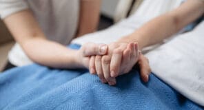 Nurse holding patient's hand in hospital bed, providing comfort and care