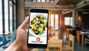 Hand holding smartphone displaying Insta Eat! app and healthy salad in a dining hall