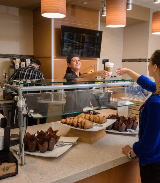 Starbucks employee serving coffee and pastries to customer in cafe