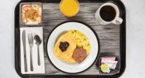 Breakfast tray with pancakes, sausage patty, scrambled eggs, coffee and orange juice