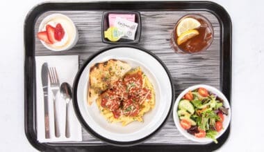 Cafeteria tray with chicken parmesan, penne pasta, side salad, iced tea, and condiments