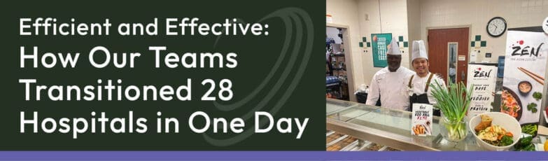 Two chefs stand behind a prepared meal counter with vegetable displays and signs about healthy eating.