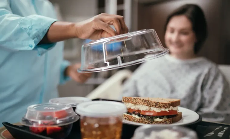 Server placing transparent cover on sandwich as smiling woman looks on in kitchen setting