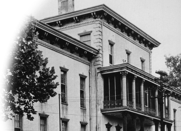 Historic black and white photo of a multi-story building with ornate architectural details and balconies