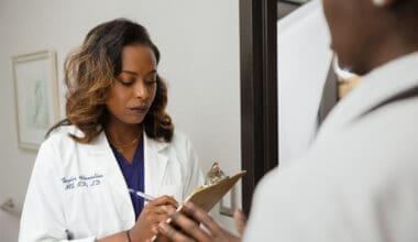 Doctor in lab coat consulting with patient and writing on clipboard