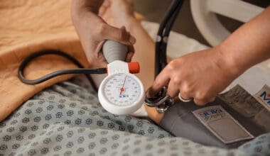 Nurse checking patient's blood pressure with sphygmomanometer and stethoscope in hospital room