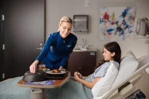 Smiling nurse serving meal to patient in hospital room