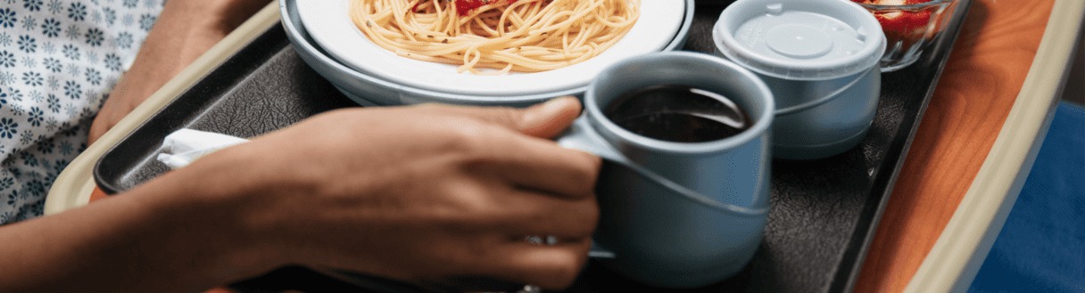 Woman's hands holding tray of spaghetti and coffee at nursing home or hospital