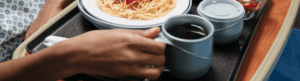 Woman's hands holding tray of spaghetti and coffee at nursing home or hospital