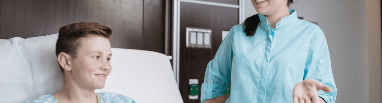 Young patient smiling at healthcare worker in teal scrubs in hospital room