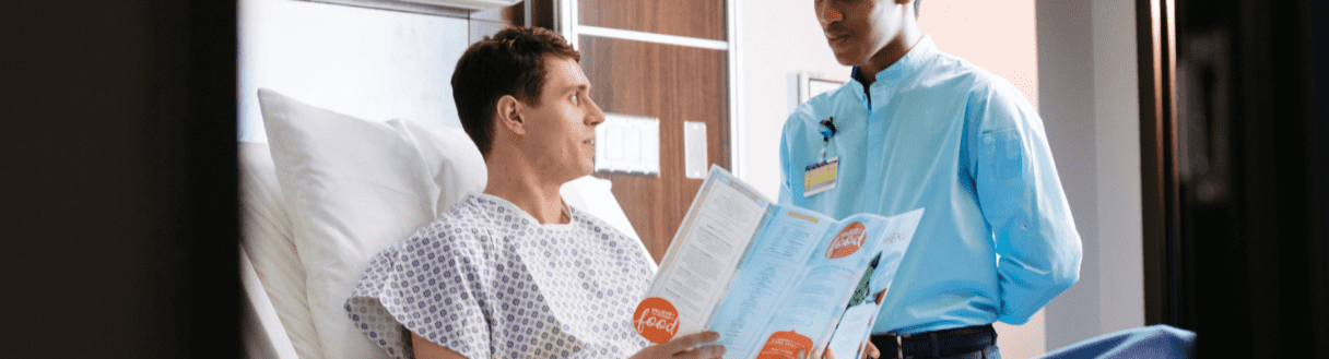 Healthcare professional talks with patient in hospital gown about nutrition facts on food packaging