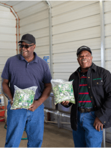 Two smiling Morrison Healthcare employees holding packaged salads at a food distribution center